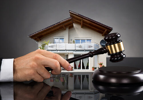 hand tapping a gavel in front of a model of a house