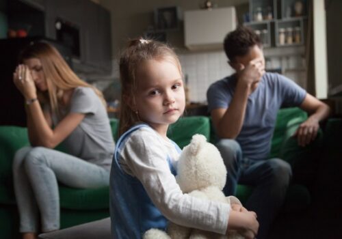 A small girl between two fighting parents in the background, needing a child custody attorney in Pekin IL