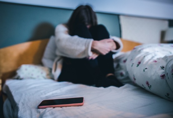 A woman sits on her bed with her arms around her legs before calling a Domestic Abuse Attorney in Pekin IL